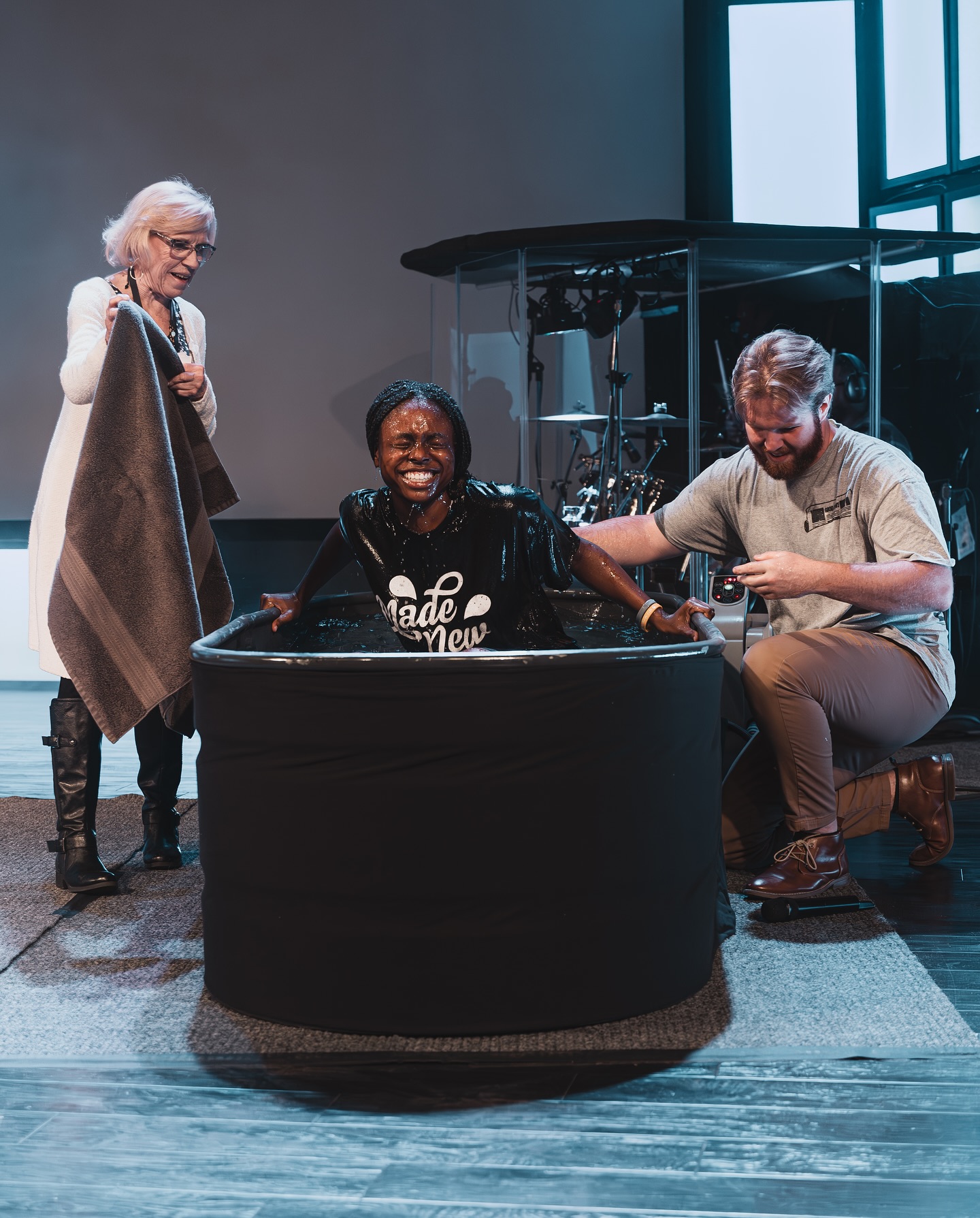A woman smiling in the baptism tank after being baptized at Stone Edge Church, with two team members beside her