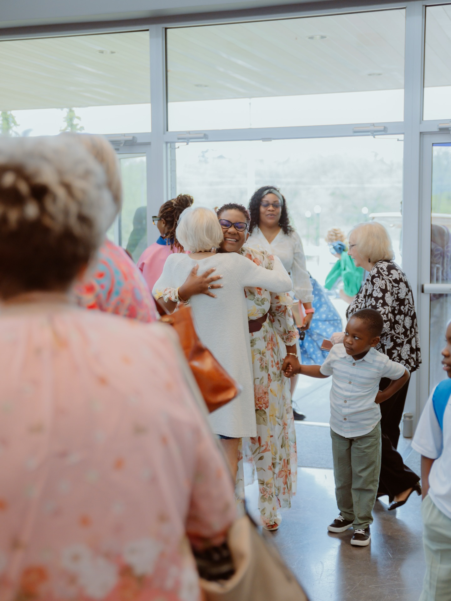 A smiling woman hugs a guest in the Stone Edge Church lobby while families gather near the entrance
